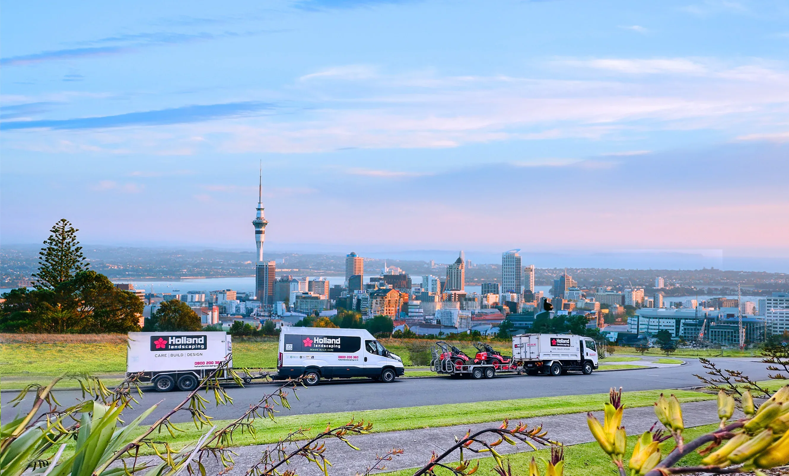 Holland Landscaping fleet on One Tree Hill with the Auckland CBD skyline at sunrise