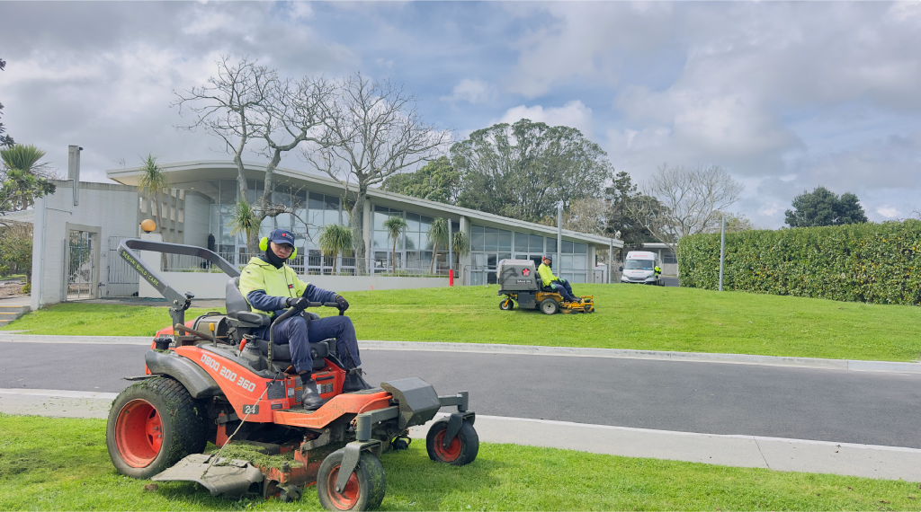 Two Holland Landscaping crew members carrying out lawn maintenance at an Auckland site using a riding mower.